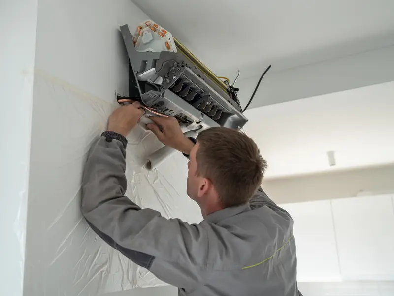 Installateur fixant un split mural lors de la pose d'une pompe à chaleur air-air