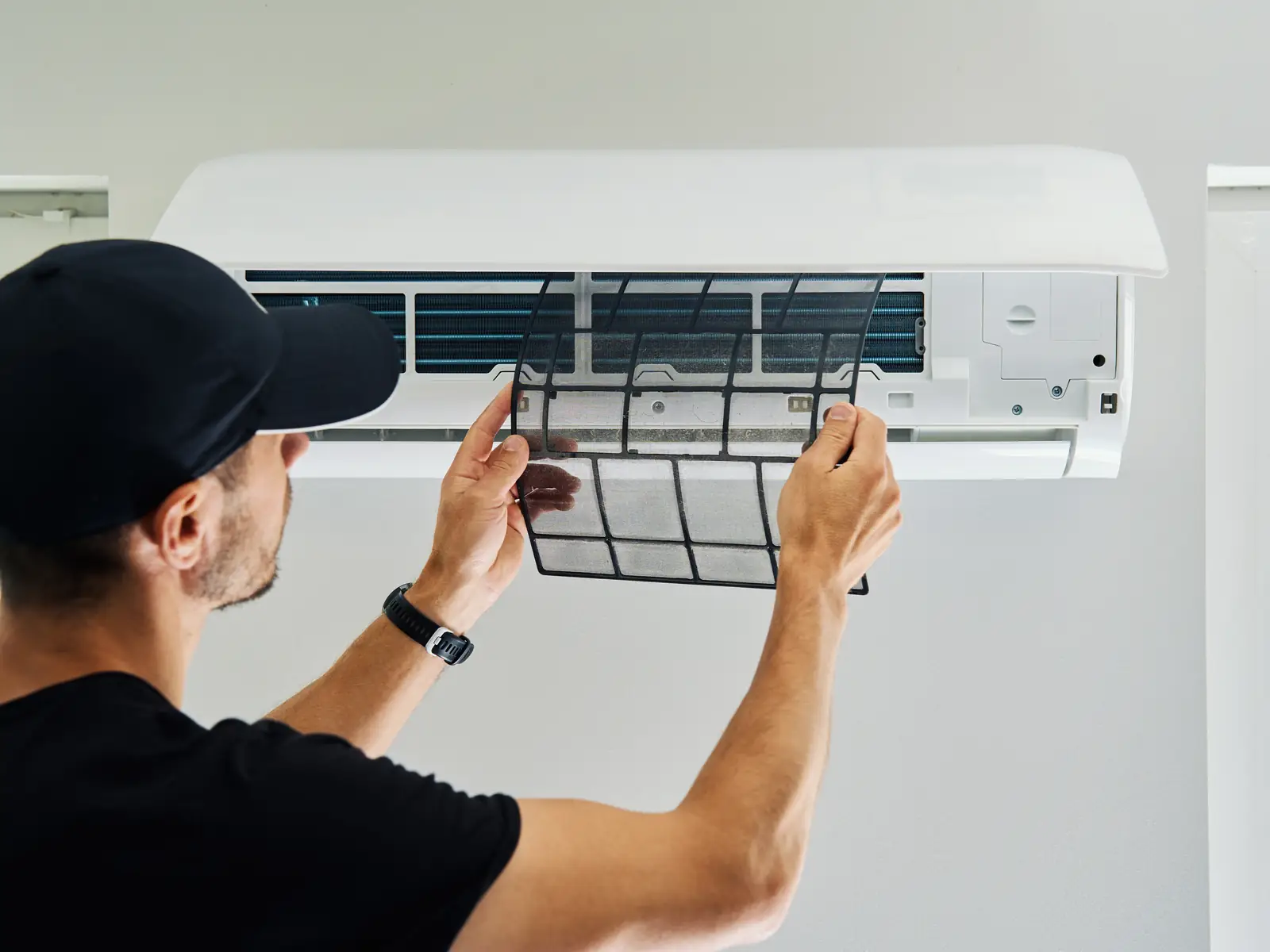 Technicien contrôlant le filtre d'une climatisation, un geste régulier pour un local ouvert toute la journée