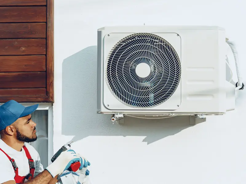Technicien intervenant sur un groupe extérieur de climatisation fixé au mur