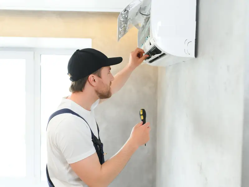 Technicien réalisant les finitions d'une climatisation murale dans un appartement